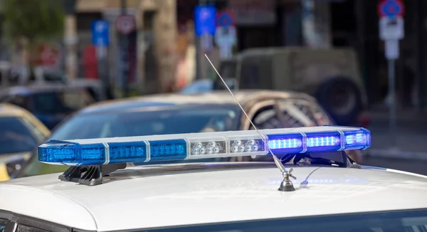 Blue light flasher at police car top closeup view, blur cityscape background. The roof mounted lightbar and siren, emergency vehicle, municipal police