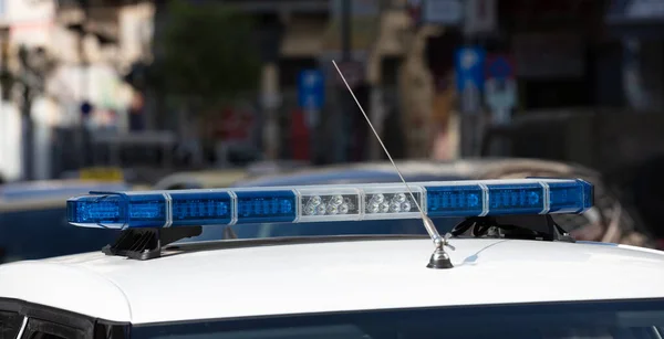 Blue light flasher at police car top closeup view, blur cityscape background. The roof mounted lightbar and siren, emergency vehicle, municipal police