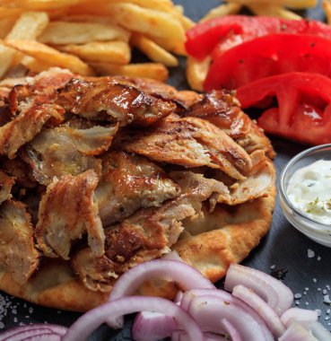 Gyros Yunan yemeği. Izgara et dilimleri kızarmış patates, domates ve yoğurtlu tzatziki ile servis edilir. Pide ekmeği, siyah taş arka plan, yakın görüş. Türk şavurması