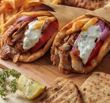 Gyros Yunan yemeklerini sarar. Kızarmış patates, domates ve yoğurt tzatziki ile dilimlenmiş ızgara et, pide ekmeği, ahşap masa arkası, yakın görüş. Türk şavurması