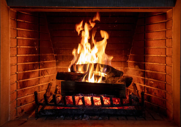 Fireplace, fire burning, cozy warm fireside, holiday christmas home. Wood logs flaming, bricks background, closeup view