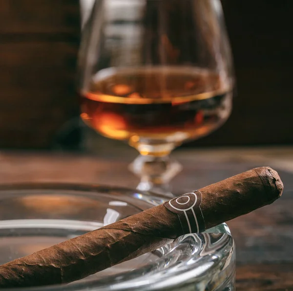 Tobacco and alcohol. Cigar and brandy on a wooden table, closeup view. Cuban quality cigar and rum, smoking and drinking luxury lifestyle