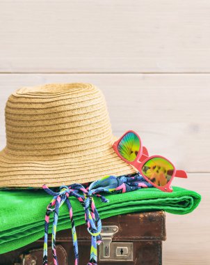 Boş ahşap arka planda plaj aksesuarlarının dikey görüntüsü. Turizm için yaz seyahati esasları, mayo, havlu, gözlük, eski bir bavula takılan şapka. Boşluğu kopyala.