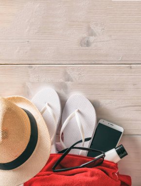 Boş tahta arka planda yaz kumsalı çantası ve aksesuarları. Yaz tatili için ekipman, şapka, havlu, parmak arası terlik, güneş gözlüğü, mobil, güneş kremi. Uzayı kopyala, şablon.