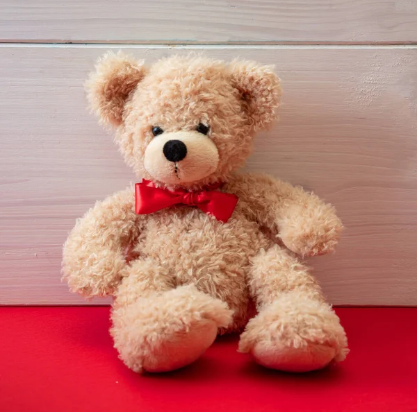 Urso Pelúcia Vestindo Laço Vermelho Sentado Chão Vermelho Fundo Parede — Fotografia de Stock