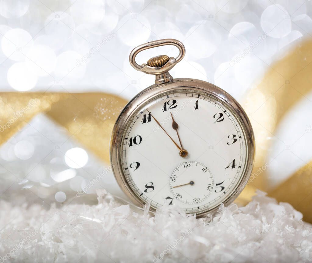 New Years eve countdown. Almost midnight on an old circle silver shiny pocket watch, bokeh background. Five minutes before twelve. Celebration, party, hope time for a better year.