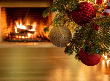 Renkli mücevherleri olan bir Noel ağacı dalı, yerdeki ışıkların yansıması, yanan şömine arka planı, fotokopi alanı. Xmas iç oda kutlama konsepti. Sıcak aile anları.