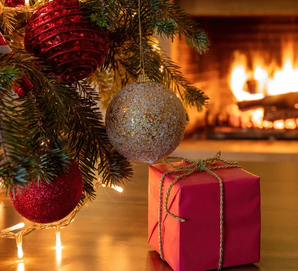 クリスマスプレゼントインテリアホームお祝いのコンセプト カラフルなボールとクリスマスツリーの枝 輝きリボン付きの1つのギフトボックス 暖炉の背景を燃やす 暖かい家族の瞬間 — ストック写真