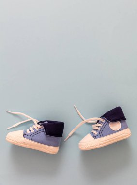 Çocuk ilk adımları atıyor. Bebek spor ayakkabıları pastel mavi arka planda yürüyor. Küçük beden ayakkabılar, branda ayakkabılar. Boşluk, kart davet şablonu