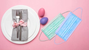 Covid19 salgınında Paskalya bayramı kutlaması. Koronavirüs koruyucu maskeler ve pembe arka planda Paskalya masası ayarları, üst görünüm.
