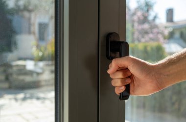 Adam metali ya da PVC kapısını açar ya da kapatır. El ele tutuşan alüminyum pencere kulpu yakın çekim görüntüsü. Enerji tasarrufu, güvenlik profili, bulanık bahçe arka planı