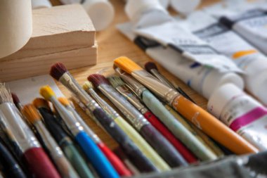 Boyama konsepti. Kullanılan boya fırçaları, ahşap masa arkasında kirli ve bulanık mizaç tüpleri. El yapımı aksesuarlar, suluboyalı sanat, çocuklar için hobi. Görüş açısını kapat.