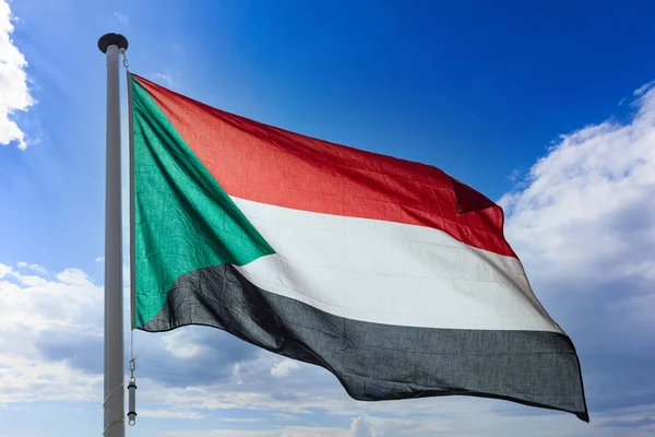 Sudan flag, Republic of Sudan national symbol on a flagpole waving against blue cloudy sky