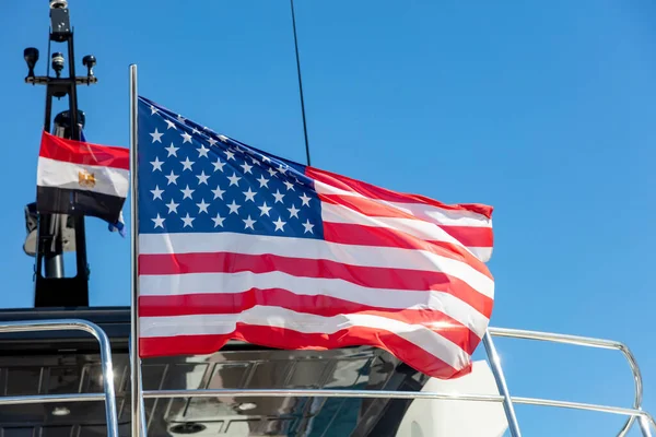 United states of America flag waving on yacht stern. Luxury boat moored at marina in Athens Greece. Blue sky background, close up view.
