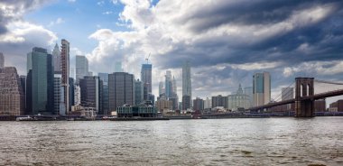 New York City ve Brooklyn Köprüsü, East River boyunca, mavi bulutlu gökyüzü arka planı. Manhattan gökdelenlerinin panoramik manzarası, Amerika Birleşik Devletleri
