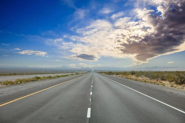 Highway in a sunny spring day, countryside USA. Empty national road going straight, crossing American desert, Blue cloudy sky background