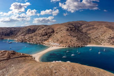 Kolona iki taraflı kumlu plaj, hava aracı manzaralı. Yunanistan, Kythnos Adası, Cyclades. Yelkenliler kıyıdan açıkta, sakin deniz, mavi gökyüzü arka planı. Yaz tatili ve Ege Denizi 'nde yelkencilik