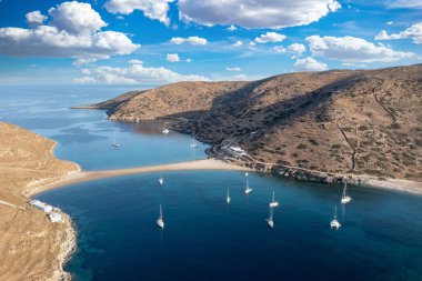 Kolona iki taraflı kumlu plaj, hava aracı manzaralı. Yunanistan, Kythnos Adası, Cyclades. Yelkenliler kıyıdan açıkta, sakin deniz, mavi gökyüzü arka planı. Yaz tatili ve Ege Denizi 'nde yelkencilik