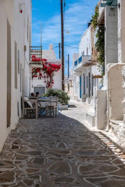 Yunanistan, Kimolos Adası. Kiklad. 18 Mayıs 2021. Chora köyünde bir kafede iki adam. Yunan geleneksel mimarisi, beyazlatılmış binalar ve dar kaldırım taşı caddeleri. Güneşli gün, açık mavi gökyüzü