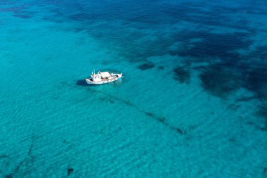 Turkuaz mavi deniz arka planında bir balıkçı teknesi. Hava aracı görüntüsü. Mavi ve beyaz geleneksel balıkçı teknesi güneşli bir günde Ege 'de dalgalı sulara demirlemiş. Yunan adaları yaz tatilleri, varış yerleri Yunanistan