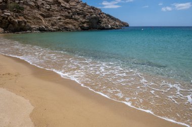 Kumsal arka planı, kumdaki yumuşak okyanus dalgası. Boş plaj, boşluk, yaz tatili kartı ve reklam şablonu. Açık mavi gökyüzü, sakin deniz arka planı. Mykonos Adası, Cyclades. Yunanistan