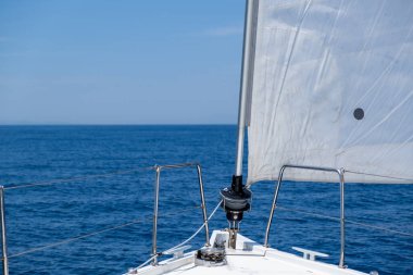 White sloop rigged yacht sailing in open calm ocean, blue sky background, sunny day. Sailboat deck, bow, mast and sails closeup view. Leisure activity, travel and transportation concept.