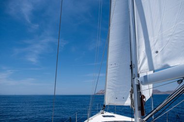 White sloop rigged yacht sailing in open calm ocean, blue sky background, sunny day. Sailboat deck, bow, mast and sails closeup view. Space, summer holidays card, advertise template.