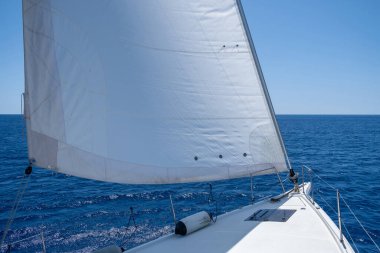 White sloop rigged yacht sailing in open calm ocean, blue sky background, sunny day. Sailboat deck, bow, mast and sails closeup view. Leisure activity, travel and transportation concept.