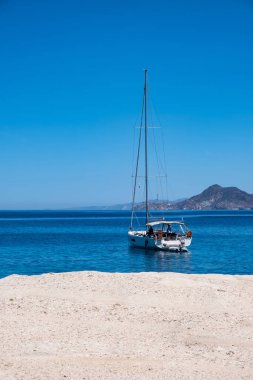 Sailboat anchored at Sarakiniko. Milos island, Greece. White chalky rock empty, calm rippled sea and clear blue sky background. Sailing in Aegean Sea, Cyclades. Smmer vacation card, space template