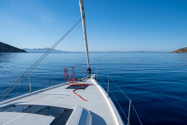 Yacht cruising in Aegean sea. White sailboat front deck part, in calm ocean, no wind, blue sky background. Space, summer holidays card, advertise template.