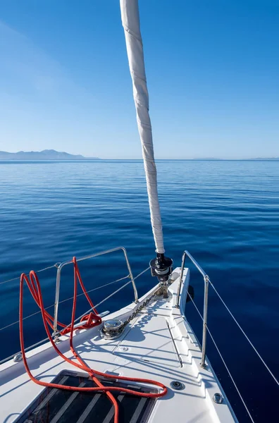 Yacht cruising in Aegean sea. White sailboat front deck part, in calm ocean, no wind, blue sky background. Space, summer holidays card, advertise template.