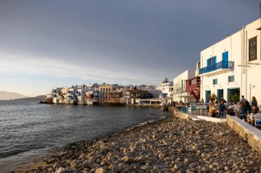 Mykonos island, Cyclades, Greece. May 20, 2021. Little Venice landmark, famous cosmopolitan destination. Traditional houses with balconies over the sea. Cafe restaurants at the seaside at sunset