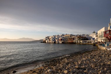 Mykonos island, Cyclades, Greece. May 20, 2021. Little Venice landmark, famous cosmopolitan destination. Traditional houses with balconies over the sea. Cafe restaurants at the seaside at sunset