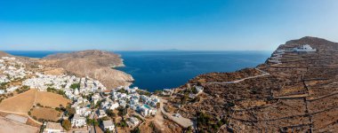 Folegandros Adası, Yunanistan, Cyclades. Chora köyü ve yokuş yukarı kilise manzarası, hava aracı manzarası. Geleneksel Kiklad mimarisi, durgun Ege Denizi üzerindeki sarp kayalıkların tepesinde beyazlatılmış binalar