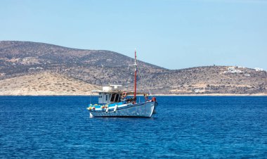 Geleneksel eski ahşap tekne sakin sulara demir atmış. Açık denize demirlemiş tipik renkli balıkçı teknesi, lo adasının arka planında. Cyclades, Yunanistan. Güneşli gün, açık mavi gökyüzü