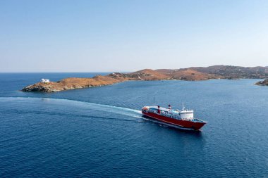 Yaz mevsimi Kea, Tzia Adası, Kiklad, Yunanistan. Korissia limanına yaklaşan bir feribot insansız hava aracı. Kırmızı renkli yolcular sakin deniz ve mavi gökyüzü arka planında gemiye biniyor. Yaz tatili kavramı