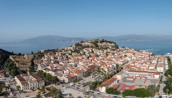 Yunanistan, Nafplio şehri hava aracı görüntüsü. Mora 'nın eski şehir manzarası, kırmızı kiremitli çatılar kayalık tepelerdeki taş kale duvarları. Mavi gökyüzü, dalgalı deniz arka planı.