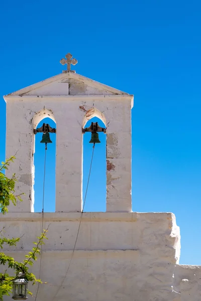 White orthodox church with religious cross on bells tower against clear blue sky background. Greek island, Cyclades Greece. Summer vacation destination.