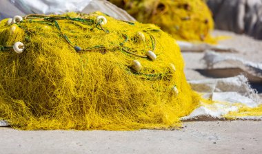 Balıkçı ağları güneşin altında kuruyan balıkçı iskelesine yığılmış. Sarı ipli ve şamandıralı balık ağları. Yunan adası Cyclades balıkçı ekipmanları.