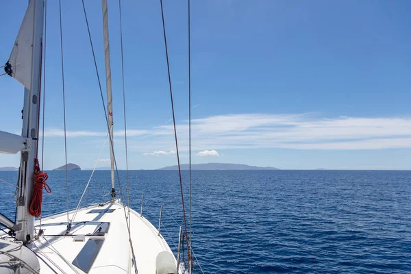 Yacht cruising Aegean Mediterranean sea. Space, summer holidays card, advertise template. White sailboat front deck part in calm ocean, no wind, blue sky and rippled sea background.