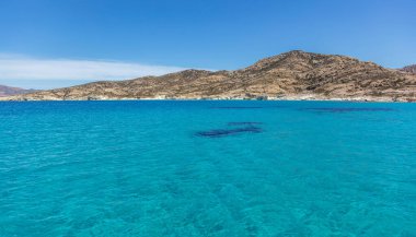 Cyclades adaları, Kimolos körfezi şeffaf su, Yunanistan. Turkuaz mavi deniz taşlı kara, açık gökyüzü arka planı, deniz manzarası. Ege denizinde yaz yüzüşü