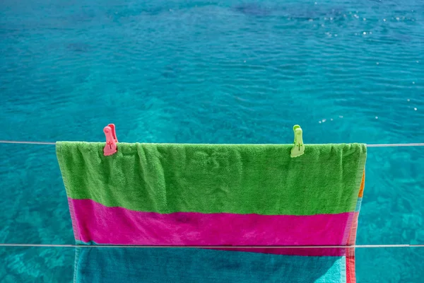 Beach towel drying on clothesline, blur sea background. Colorful towel hanging on boat stainless rail. Summer vacations and sailing, clothes wash and dry. Space, advertise template