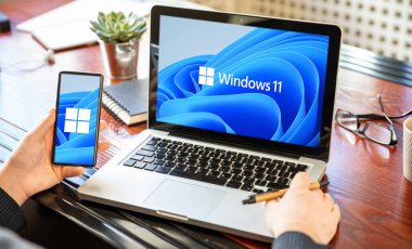 Yunanistan, 8 Temmuz 2021. Bilgisayarı ve akıllı telefonu olan bir adam, Windows 11 ekranlarda yeni Microsoft işletim sistemi, iş masası geçmişi.