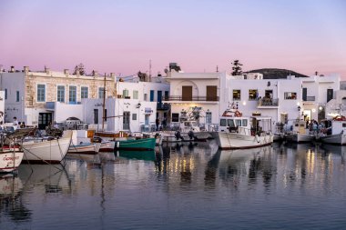 Yunanistan, Paros Adası Naousa eski limanı. Kiklad. 19 Mayıs 2021. Limandaki limanda demirlemiş tipik balıkçı tekneleri. Geleneksel açık kafedeki insanlar ve gün batımında restoranlar. Sakin deniz, yaz tatili