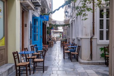 Syros Adası, Cyclades, Yunanistan. 26 Mayıs 2021. Geleneksel boş kafe masaları, Ermoupolis 'in başkenti Siros' un kaldırım taşı caddesinde sandalyeler veya Syra kasabasının arka planında. Yaz tatili.