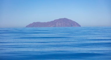 Ege Denizi, durgun su yüzeyi, berrak gökyüzü. Durgun mavi okyanus, Yunan adası kayalık kara ve mavi gölgelerde seyrediyor. Yunanistan, Kiklad. Yaz tatilleri konsepti, boşluk, şablon