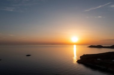 Sakin deniz suyunun üzerine gün batımı turuncu rengi. Ege Denizi, Yunanistan 'da dramatik büyülü gündoğumu deniz manzarası. Ada silueti ve dalgalı suda altın yansımalar. Cyclades adaları, hava aracı görüntüsü.