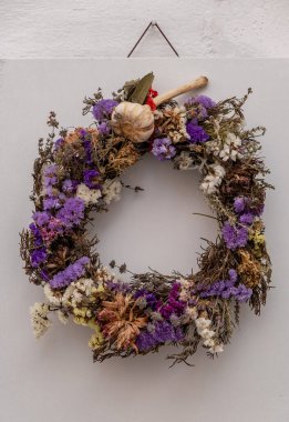 Kuru çok renkli çelenkler beyaz tahtaya yapışmış, sarımsak nazara karşı. Paros adasındaki çiçeklerle çember süsleme, Naoussa köyü Kiklad Yunanistan 'da yaz güneşli bir gün. Dikey