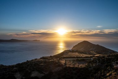 Ege Denizi üzerinde gün batımı. Güneş ışığı renkleri sarı ve turuncu Milos adasında mavi gökyüzü, Kiklad Yunanistan. Son güneş ışınları parıldıyor denizi altın dağı, yaz gecesini egzotik tatil köyü yapıyor..