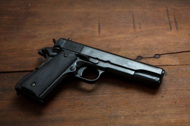 Tahta arka planda 9mm 'lik tabanca. Siyah metal silah, ordu için otomatik tabanca ve klasik bir masada güvenlik. Yan görünüm